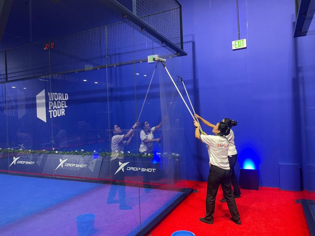 Professional cleaners performing high-reach glass wall deep cleaning at an indoor sports facility center padel in Dubai.