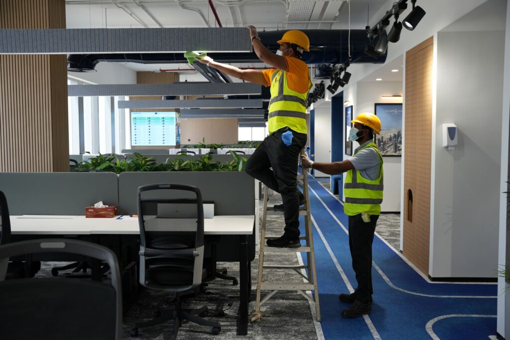 Two cleaning staff in Dubai, one holding a 5-step ladder and the other cleaning a ceiling light fixture our professional deep cleaning service in Dubai