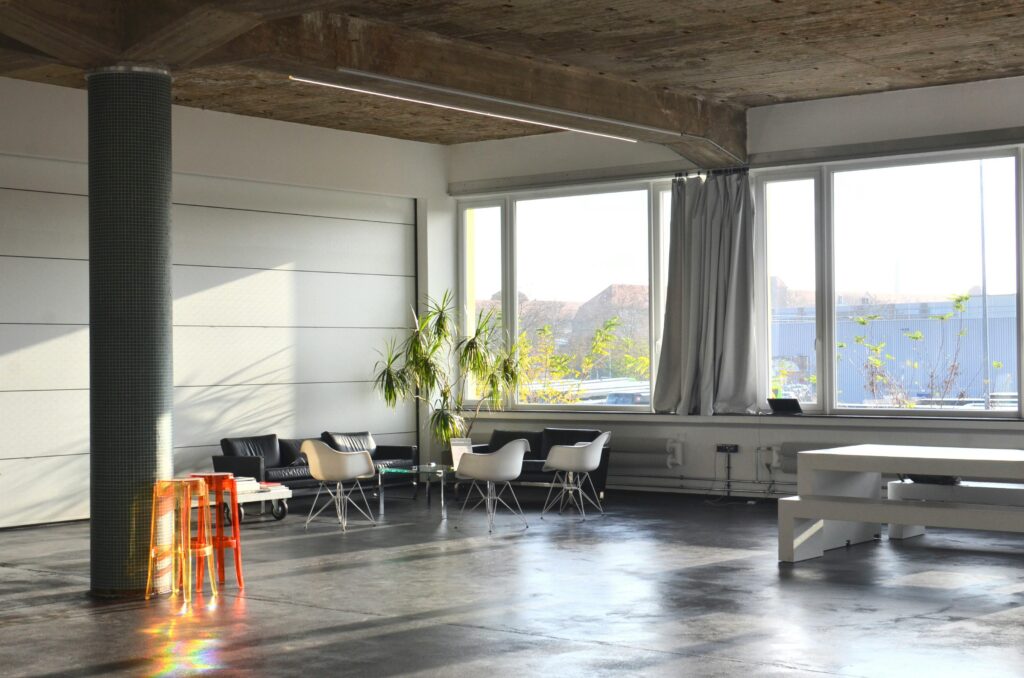 Interior of modern spacious room with column and couches placed near big window with curtains near table in light studio